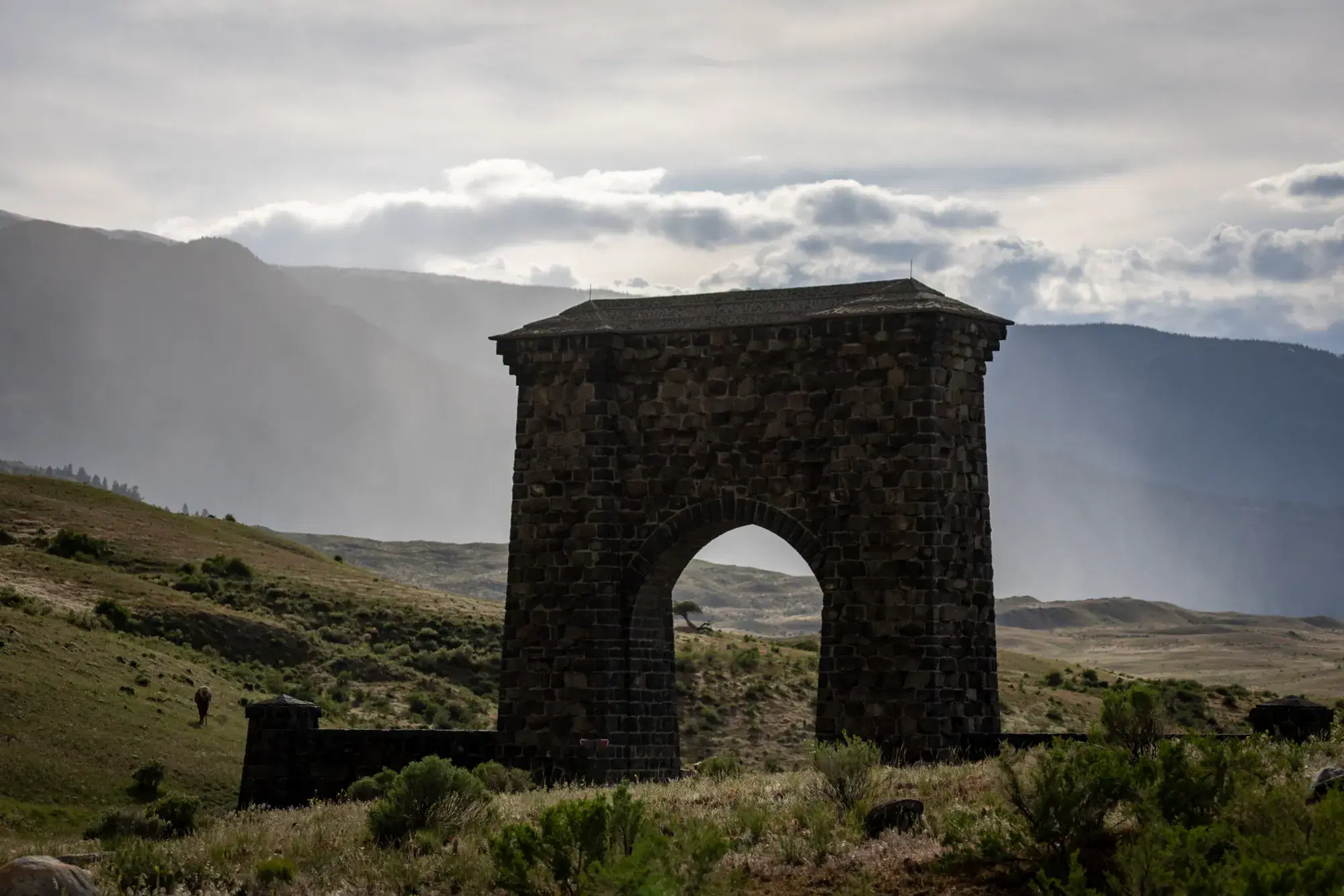 The stone Roosevelt Arch at Yellowstone's North Entrance under a stormy sky